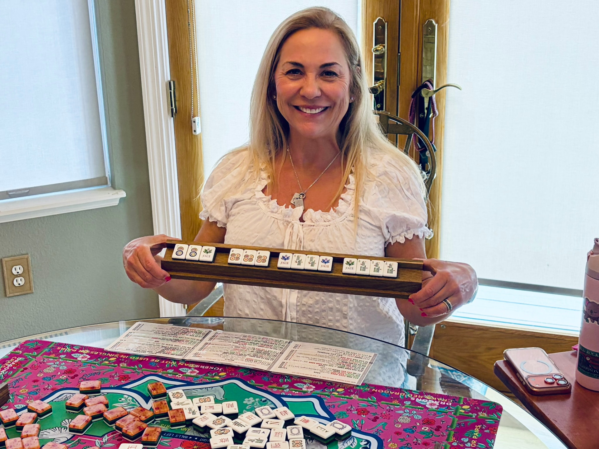 Amy Rosewater holding a Mahjong rack with tiles across a colorful Mahjong table