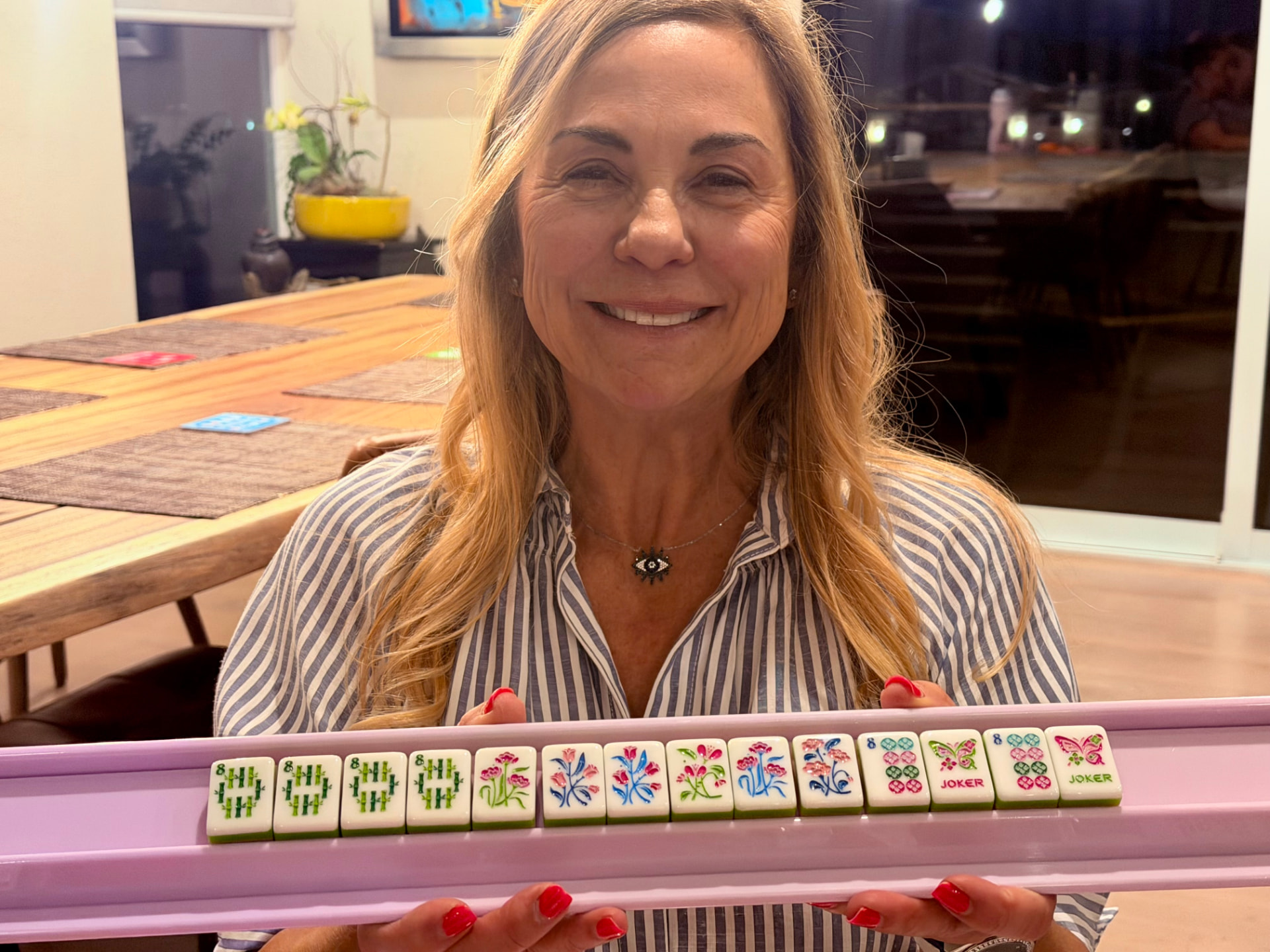 A happy player holding up her purple rack of Mahjong tiles