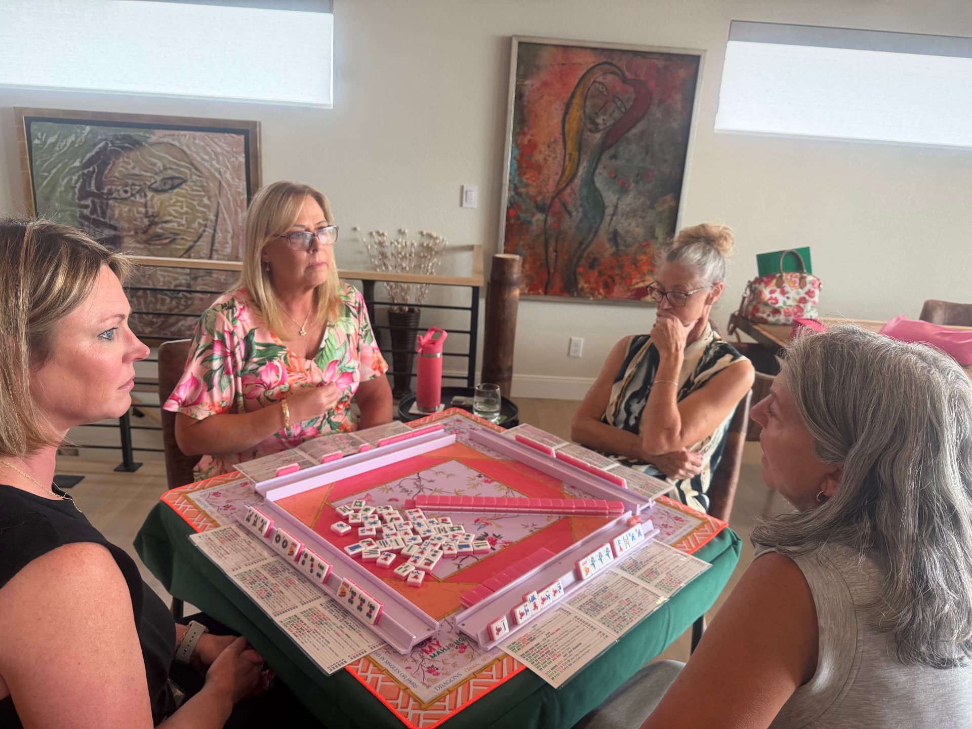 Four players mid-game around a Mahjong table with pink racks